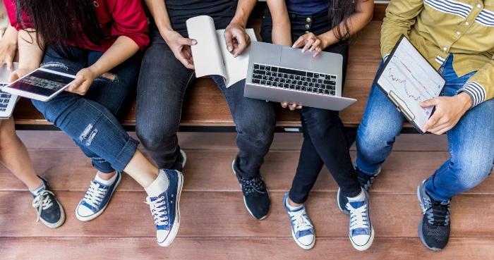 Top view of various students using laptops, tablets, and books